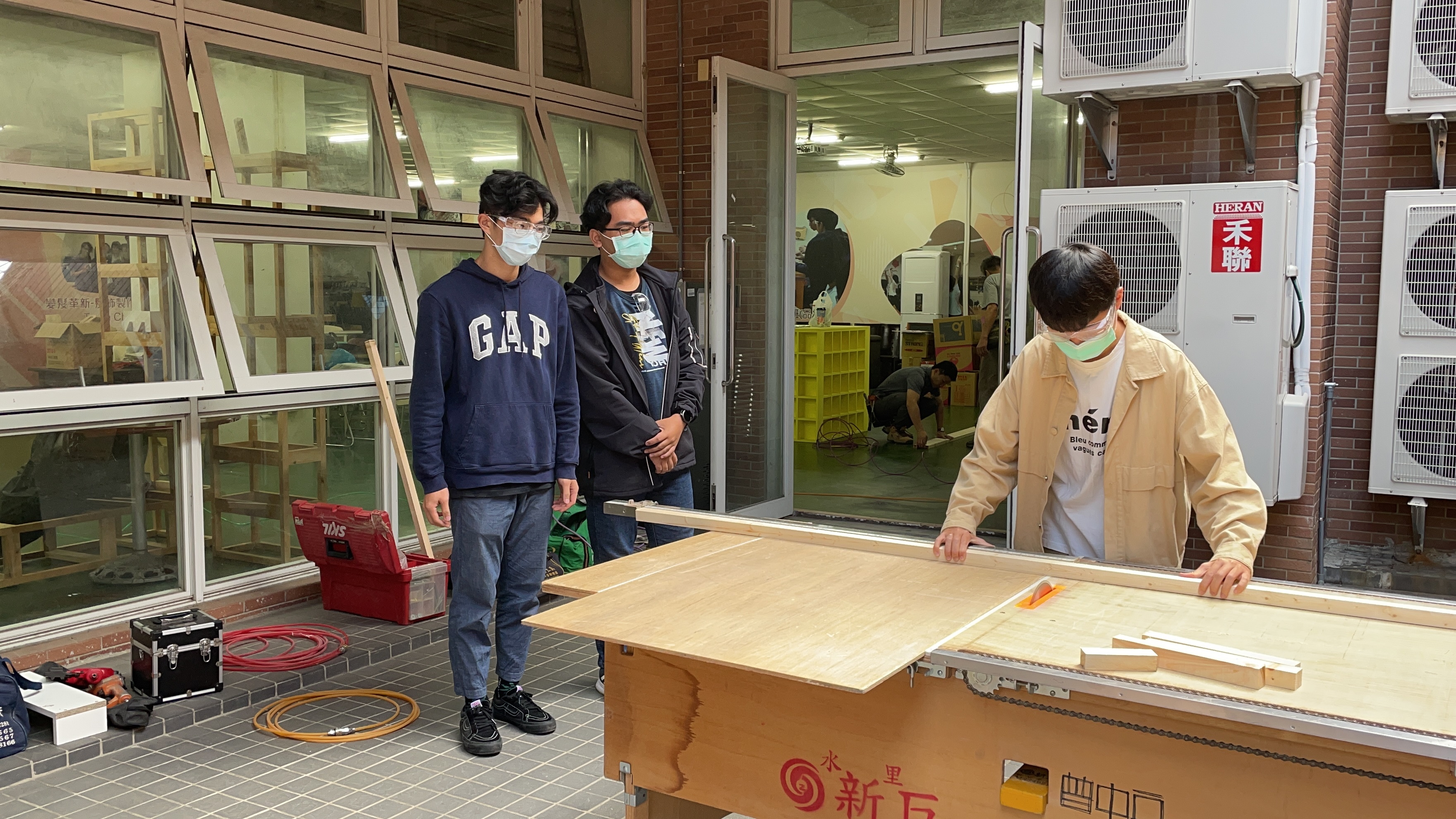 参加改造登峰学苑交谊厅的学生们，由专业木工师傅教导下学习用机器裁切木条。